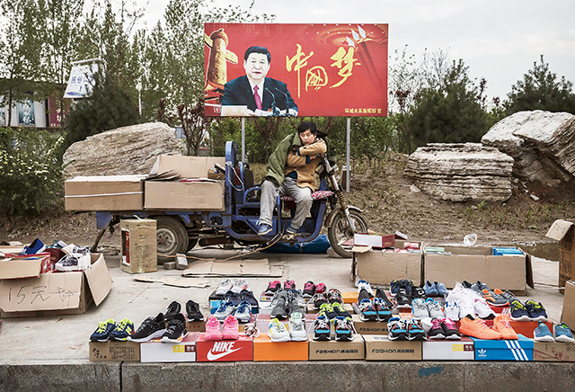 2017年4月9日中國河北省石家莊市一名攤販在展示中國國家主席習近平「中國夢」看板前的街道上販售運動鞋。Getty Images