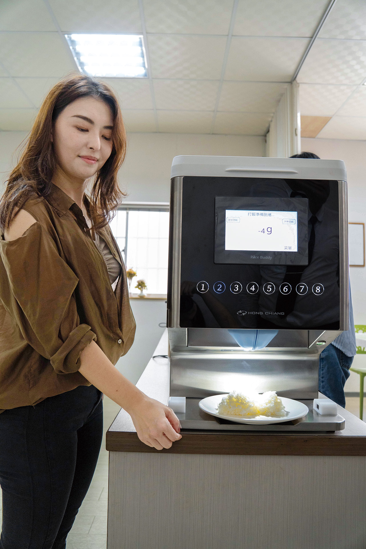 鴻匠科技董事長夫人陳采翎展示「盛飯機」，可依據店家餐食設計，送出不同克數的飯量，目前已有連鎖店採用。謝平平攝影