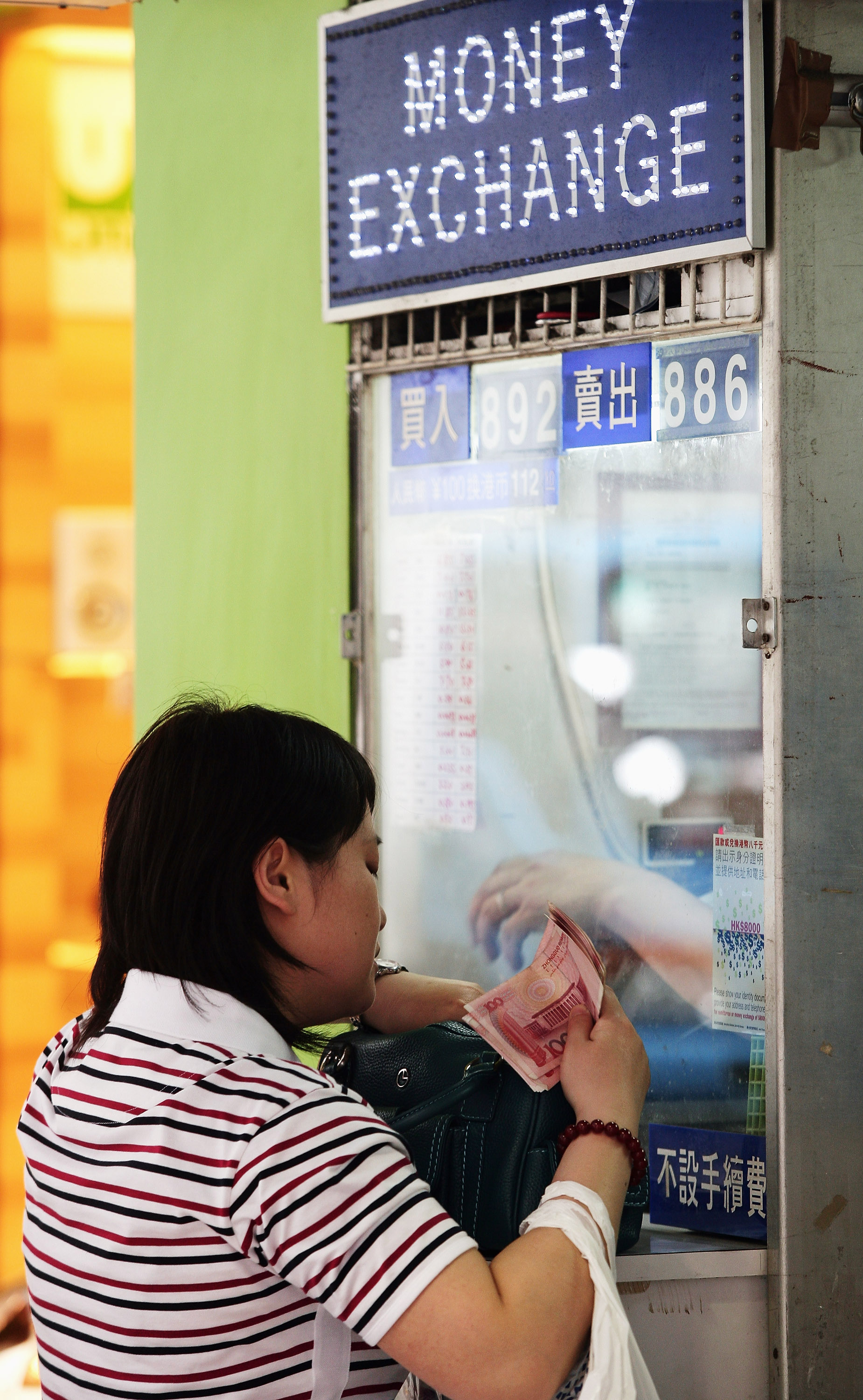 美国金融风暴席卷全球，中国也无法幸免。图为一手持百元人民币的中国妇女在外汇买卖柜台前。